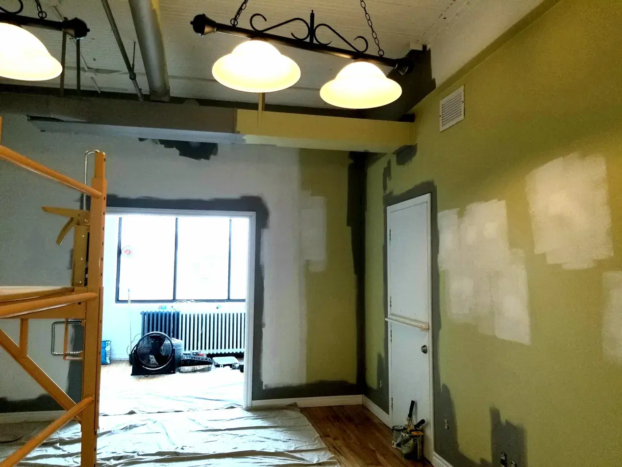 Before: olive walls mid-repaint, exposed ceiling ductwork, prep materials on the floor
